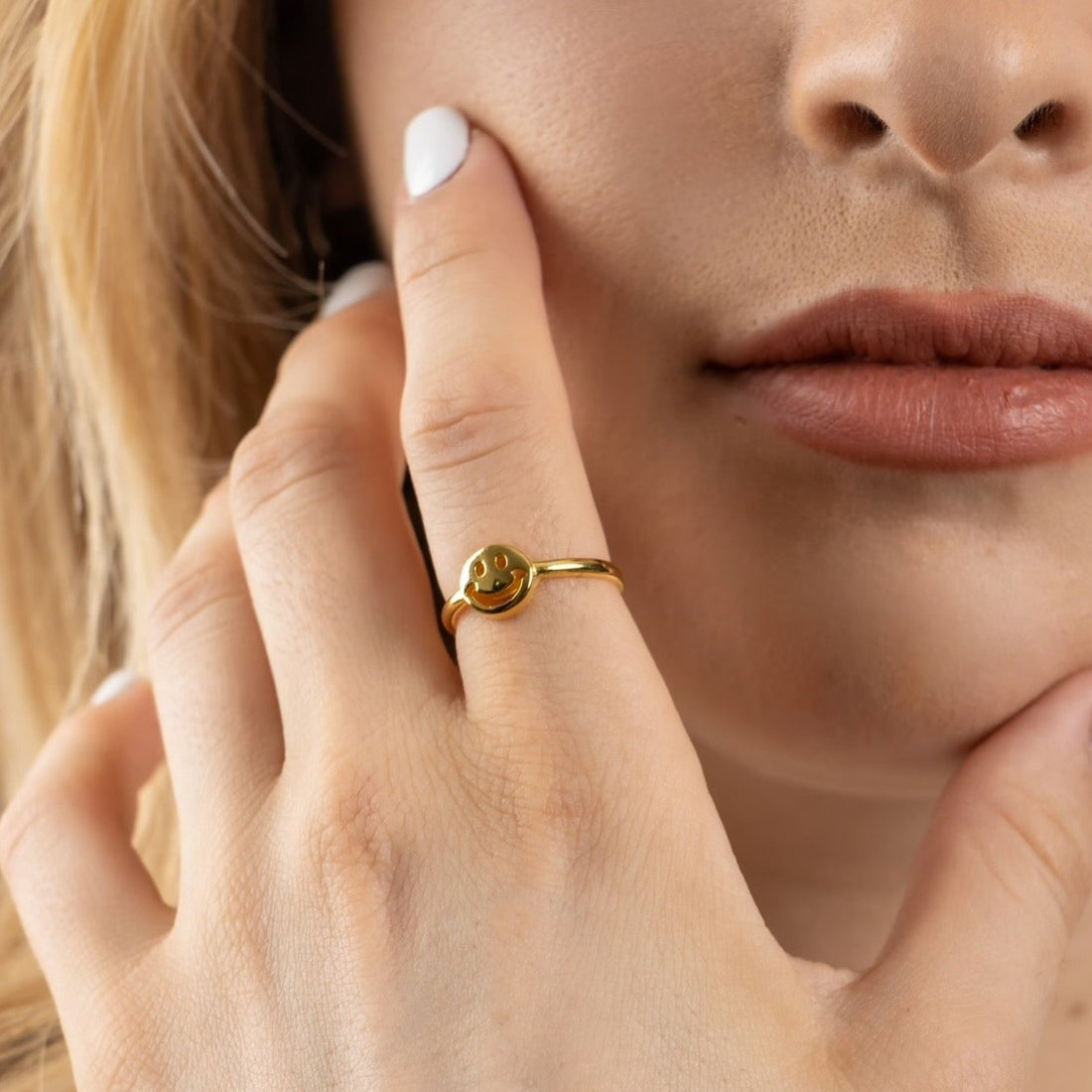 Mujer modelando anillo delgado en chapa de oro con simbolo en forma de carita feliz aplanado.